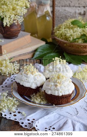 Chocolate Capcakes With Vanilla Cream Sprinkled With White Chocolate And Elderberry Flowers. Vintage