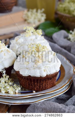 Chocolate Capcakes With Vanilla Cream Sprinkled With White Chocolate And Elderberry Flowers. Vintage
