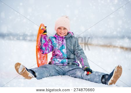 C ute girl in winter ski outfit with saucer sled on the snow