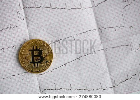 Bitcoin Is Alive. The Gold Coin Lies On A Paper Cardiogram Sheet Of People Heartbeat