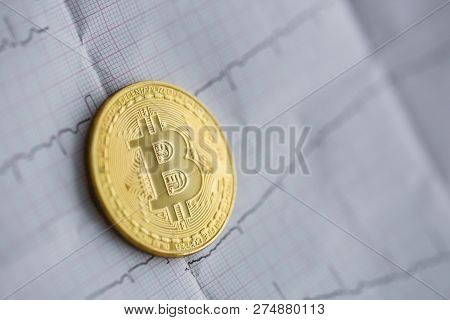 Bitcoin Is Alive. The Gold Coin Lies On A Paper Cardiogram Sheet Of People Heartbeat