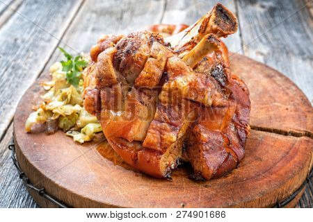 Traditional Bavarian schweinshaxe with coleslaw and preztel as closeup on a wooden cutting board 