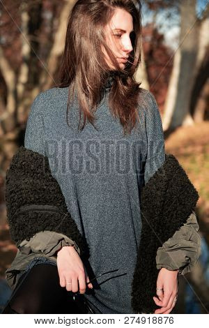 Attractive young woman wearing gray dress and hakki jacket with long fair hair posing outdoor in autunm or spring park over nature outdoor. Beautiful caucasian model portrait.