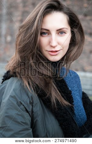 Attractive young woman wearing gray dress and hakki jacket with long fair hair posing outdoor. Beautiful caucasian model portrait.