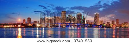 Panorama de horizonte de ciudad de Miami al anochecer con rascacielos urbanos y puente sobre el mar con reflexión