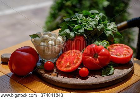 Ingridients for traditional italian salad caprese - tomato, bazil and mozzarella on wooden plate. Shot on a sunny day outside