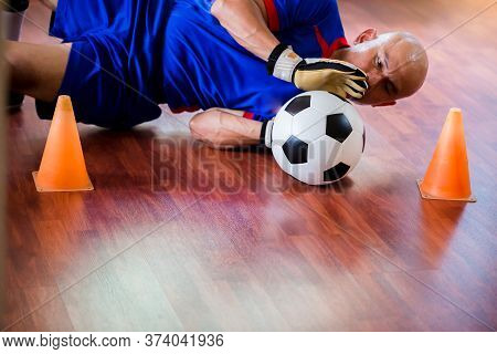 Ball In Hands Of Futsal Goalkeeper On Wooden Futsal Floor. Indoor Soccer Sports Hall.