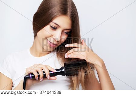 Young Woman With Luxurious Hair Straightens It With A Curling Iron