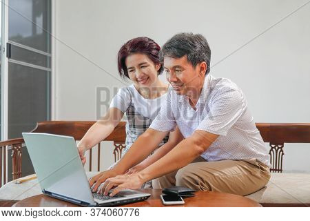 Middle Aged Asian Couple Using Laptop At Home