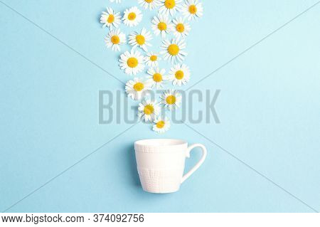 White Cup And Chamomile Flowers On A Blue Background. Chamomiles Come Out Of The Cup Like Steam. Cha