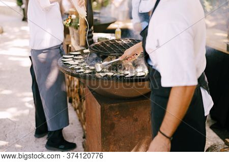 The Cook Roasts The Courgettes. Grilled Vegetables. Round Bowl-shaped Grill With A Fire Inside.