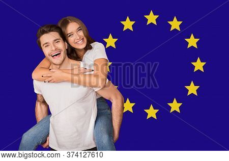 Immigration In Eu. Portrait Of Happy Young Couple Posing Over Europe Union Flag, Celebrating Europea