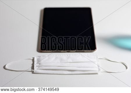 Close up of a tablet and white face mask protection against pandemic coronvirus covid 19 and for safety lying on a white table 