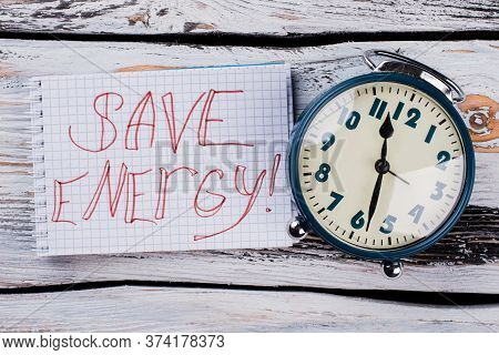 Save Enegry Tagline And Alarm Clock. White Wooden Table Surface On The Background.