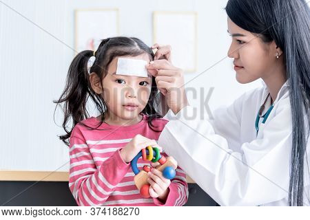 Asian Pretty Woman Doctor Is Pasting A Fever Reducing Gel Forehead Area Of A Girl Patients To Reduce