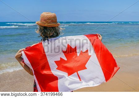 Woman In Hat With Canada Flag At The Beach. Girl Holds An Canada Flag While Standing On The Beach, B