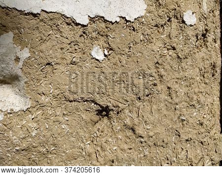 Close-up Background Of The Wall Of An Old House Made Of Clay Mixed With Straw. Old Type Of Construct
