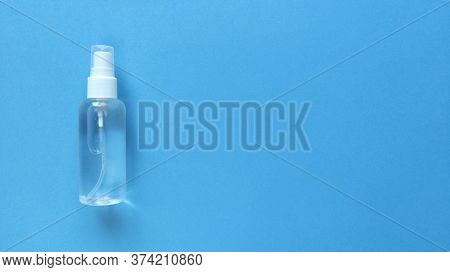 Hand Sanitizer Transparent Bottle With Spray Cap At The Left Of Blue Background. Simple Flat Lay Wit