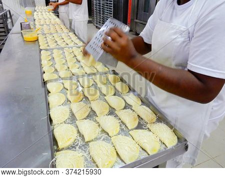 Brazilian snacks, roasted pastel, Brazilian snacks factory grating cheese in pastels before going to the oven
