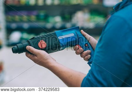 A Man Holds An Electric Drill In His Hand For Drilling. A Buyer In A Hardware Store Selects A Produc