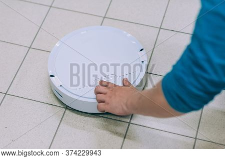 Man Turns On A Smart Robot Vacuum Cleaner On A Tile Floor.