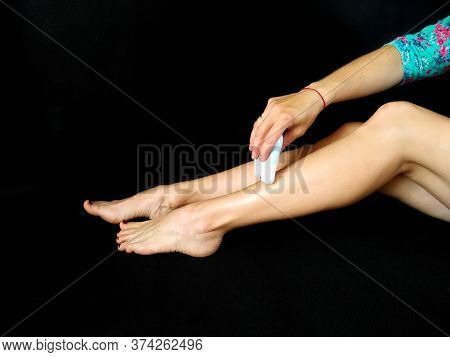 Girl In Makes Hair Removal At Home With White Epilator On Legs At Home. Isolated On Black. Selfcare 
