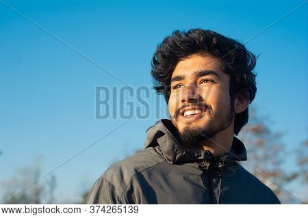 A Handsome Smiling Young Man Looking Away From The Camera In A Winter Evening. Few Trees And A Clear