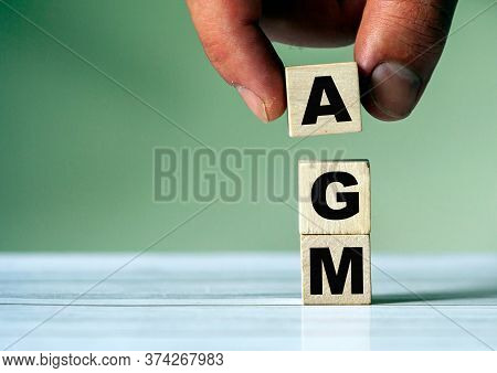 The Hand Puts The Cube Block With The Inscription Agm. Annual General Meeting - Acronym On Wooden Cu