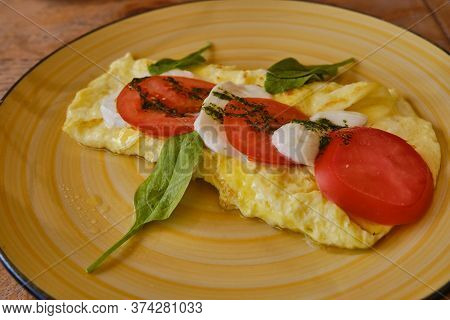 Breakfast On A Round Yellow Plate. Omelet And Ingredients Of Italian Caprese Salad. Cliced Fresh Moz