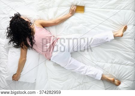 Top View Of Drunk Female Sleeping On White Bedding Holding Alcohol Bottle. Young Woman Resting After