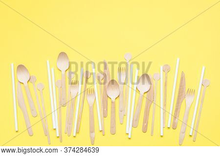Set Of Wooden Cutlery And White Paper Straws Scattered On A Yellow Background. Ecological Product. E
