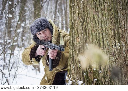 soldier in old coat and fur hat standing with a gun in the winter forest