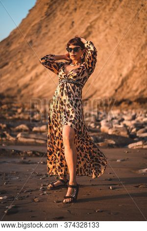 Summer Lifestyle On A Beach Next To Rocks Of A Young Brunette Caucasian Woman In A Leopard Dress By 