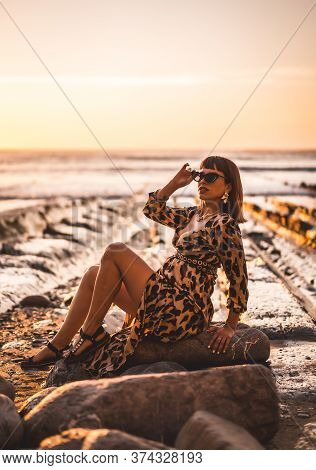 Summer Lifestyle On A Beach Next To Rocks Of A Young Brunette Caucasian Woman In A Leopard Dress By 