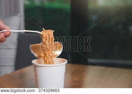 Hand Of A Man Holding A Plastic Fork With Cooked Instant Noodles. A Cup Of Instant Noodle With Fork 