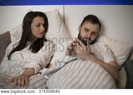 Young Married Couple Laying In Bed, Handsome Man Using Mobile Phone Checking Social Network Ignoring
