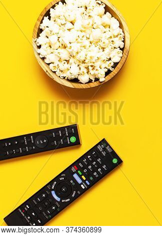 Black Tv, Audio Remote Control And Popcorn On Bright Yellow Background Flat Lay Top View Copy Space.