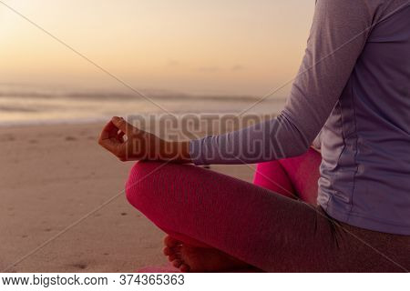 Mid section view of a Caucasian woman wearing sports clothes, enjoying time at the beach on a sunny day, practicing yoga, meditating in lotus position