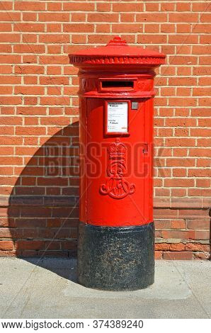 Felixstowe, Suffolk, England - June 26, 2020: Red Post Box Isolated Against Brick Wall.