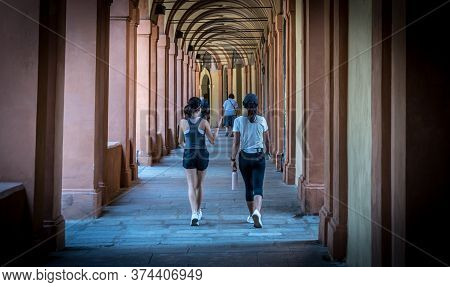 Mother In Black Hat And Daughter Walking Down Promanade In Sneakers And Shorts And Pants In Bologna 