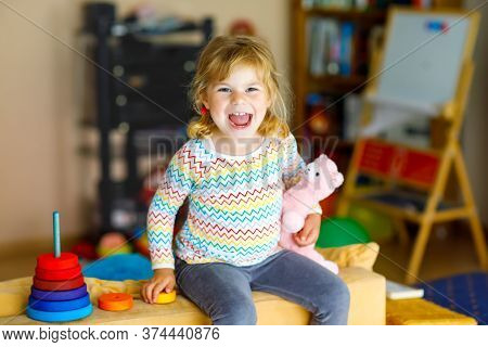 Cute Little Toddler Girl Playing Alone With Colorful Wooden Rainbow Pyramid And Toys At Home Or Nurs