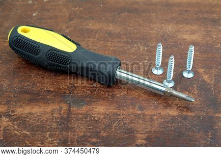 Handy Screw Driver And Three Sharp Screws On Brown Wooden Background Closeup View