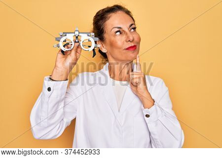 Middle age senior oculist woman holding optometrical glasses for vision correction serious face thinking about question, very confused idea