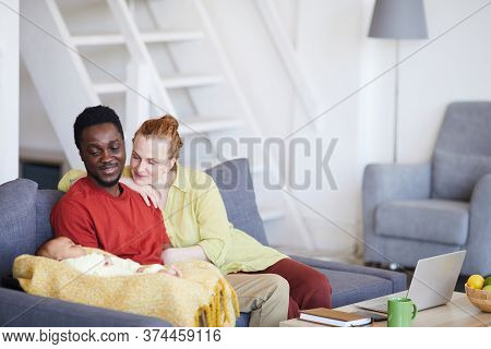 Young Parents Sitting On Sofa And Looking At Their Baby While He Sleeping They Sitting On Sofa In Th