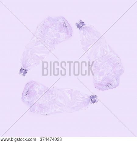 Three Crashed Plastic Bottles On Violet Background Form Resycling Sign. Plastic Utilisation Concept.
