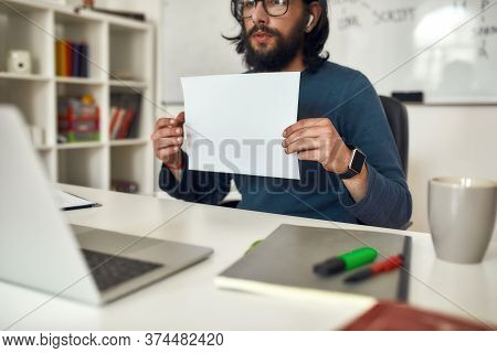 Cropped Shot Of Male Teacher Wearing Eyeglasses Showing A Blank Sheet Of Paper At Web Camera While G
