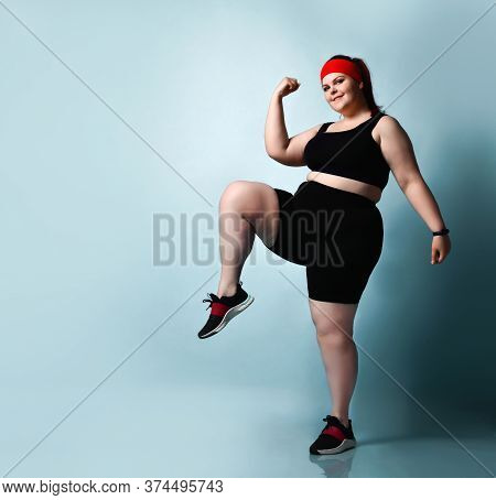 Active Smiling Plus-size Girl Practices Exercises Stepping In Place Raising Up Knees High On Blue Ba
