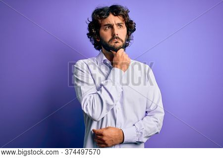 Young handsome business man with beard wearing shirt standing over purple background Thinking worried about a question, concerned and nervous with hand on chin