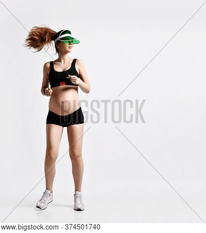 Pregnant Girl With Belly, In Green Sun Visor, Black Sport Shorts And Top, Pink Sneakers. She Is Jogg