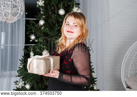 Very Happy Pretty, Beautiful, Young Woman Near Christmas Tree Smiling And Holding A Gift